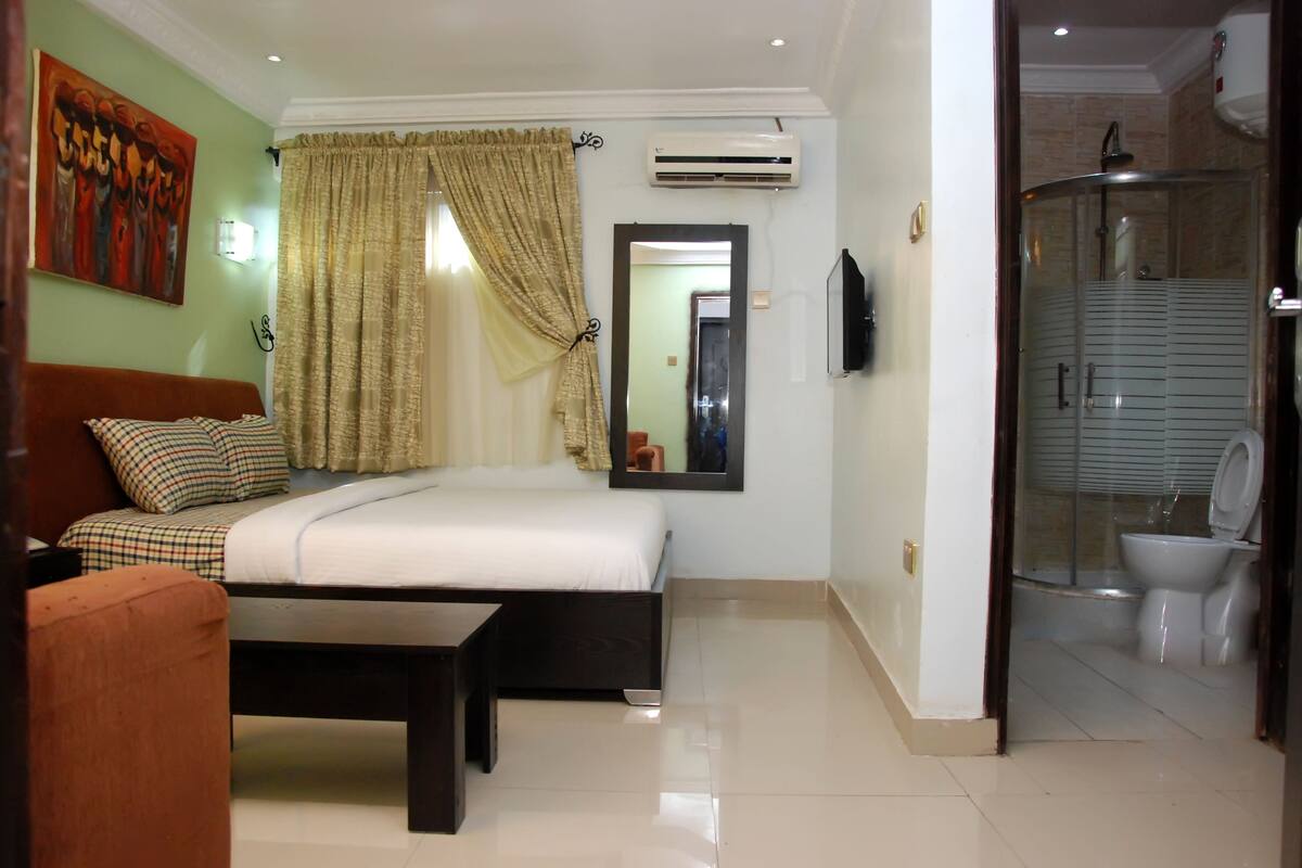 Quarto com cama, sofá, espelho, ar condicionado e chuveiro.