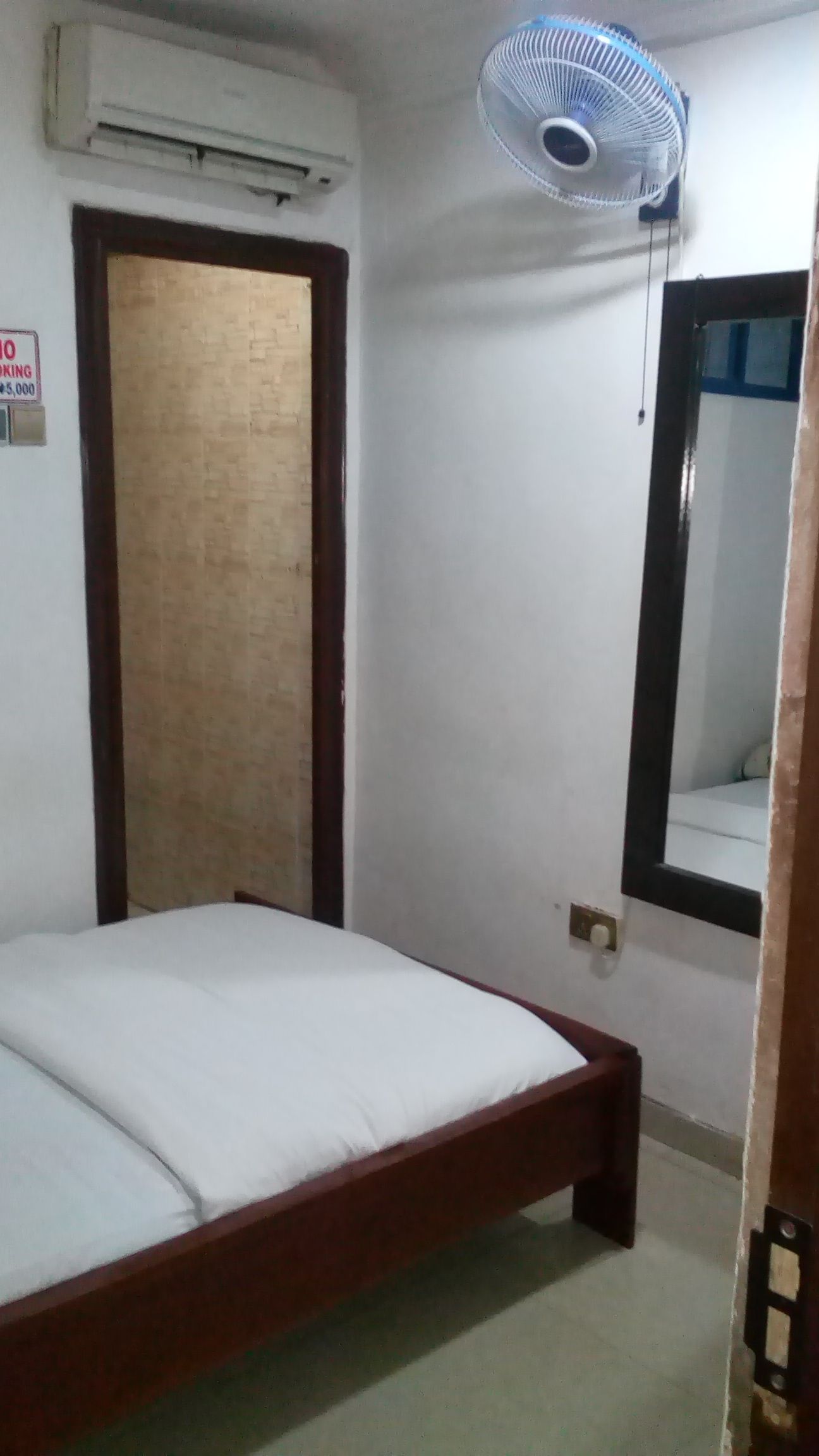 Una habitación con cama, aire acondicionado, ventilador de pared y una puerta.