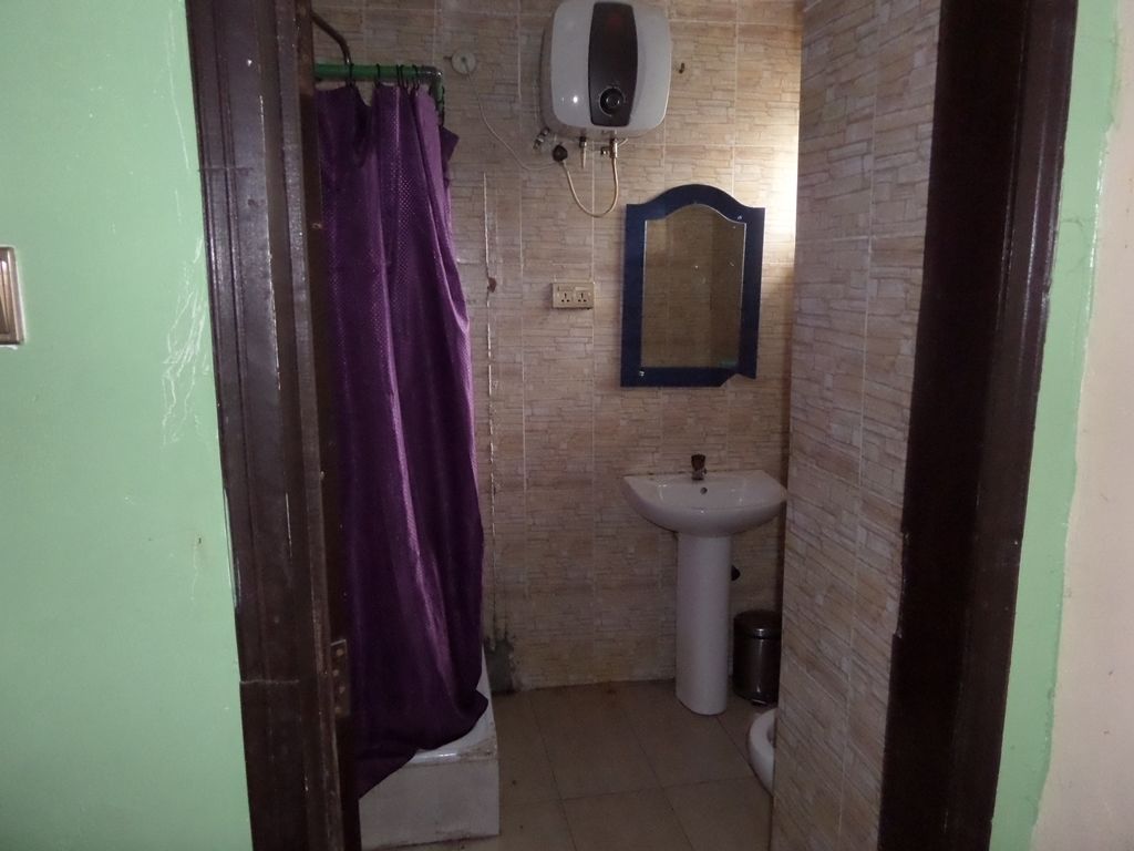 A small bathroom with a purple shower curtain, a white pedestal sink, a mirror, and a hand dryer.