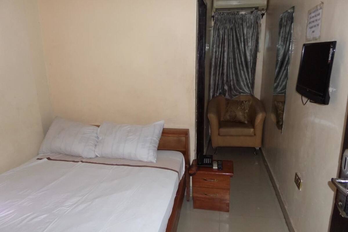 Quarto com cama, cadeira, mesa de cabeceira, televisão e cortina.