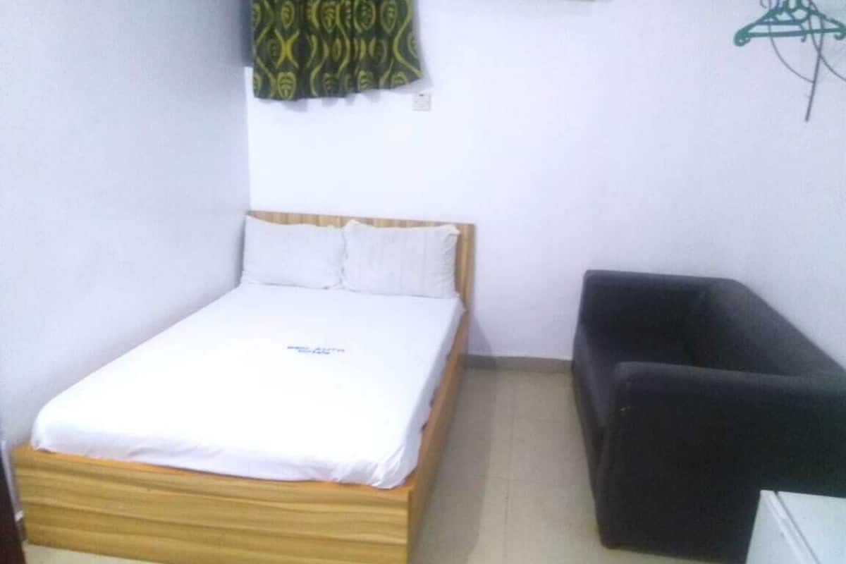 Quarto com cama, sofá escuro e pequeno armário branco.