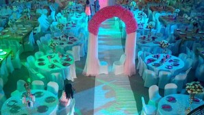 A banquet hall with round tables and white chairs, a central archway, and a stage with a pink backdrop. - BEN AUTO guest house (Lagos)