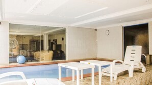 A pool area with lounge chairs, a table, and a glass wall reflecting the interior. - BEN AUTO guest house (Lagos)