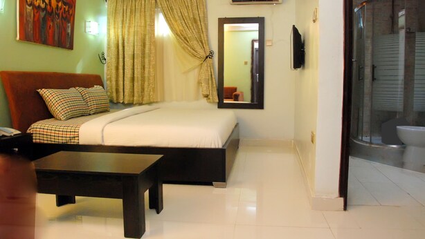 A bedroom with a bed, bedside table, and a shower area. - BEN AUTO guest house (Lagos)