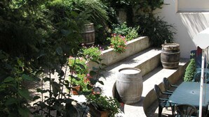 Un área de patio con una mesa y sillas, rodeada de macetas y barriles con plantas.