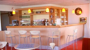 Zona de bar con mostrador, sillas y estanterías llenas de botellas y vasos.