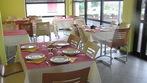 Un restaurante con mesas dispuestas para comer, sillas y ventanas amplias.