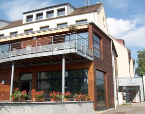A modern building with a balcony, large windows, and potted plants. - Centre Le Mittel (Mittelwihr)