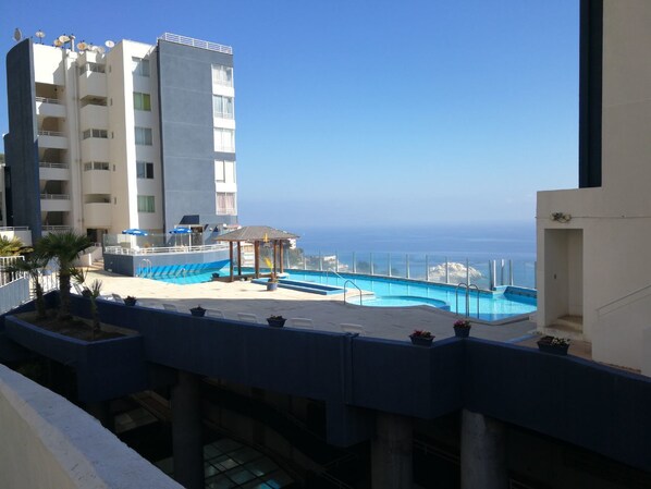 A rooftop pool with a clear view of the ocean, surrounded by a modern building with balconies. - Departamento Euromarina (Vina del Mar)