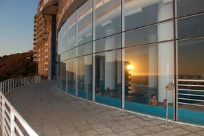 A modern building with a glass facade overlooking a pool area. - Departamento Euromarina (Vina del Mar)