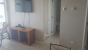 A living room with a flat-screen TV mounted on the wall, a wooden entertainment unit, and a dining area with a chair and table. - Departamento Euromarina (Vina del Mar)