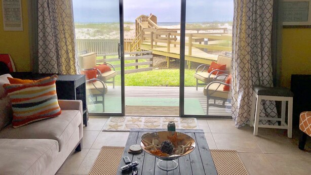A living room with a large sliding glass door leading to a deck with a view of a beach and a wooden staircase. - Mayo Clinic under 15 min (6 miles), Beach under 2 min walk (Jacksonville Beach)
