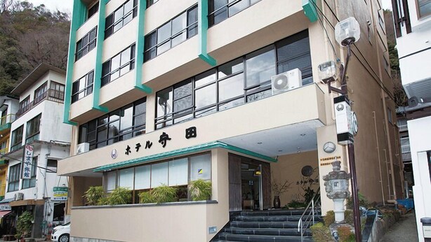 A multi-story building with a beige facade, green accents, and a sign indicating it is a hotel. - Hotel Morita (Minobu)