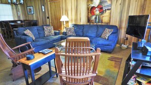A living room with a blue sofa set, a wooden rocking chair, a coffee table, and a television on a stand.