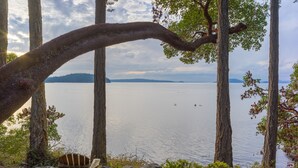 Une vue sur le lac, avec deux fauteuils Adirondack et un banc en bois, le tout entouré de rochers et d’arbres.
