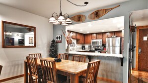 A modern kitchen with wooden cabinets, stainless steel appliances, and a dining area with a wooden table and chairs.