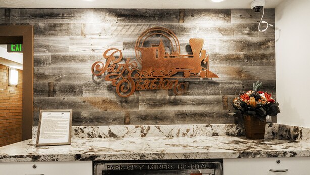 A reception desk with a rustic wooden backdrop, a metal sign reading "Park City Station," and a bulletin board with a menu.