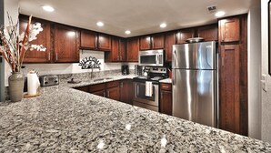 A modern kitchen with granite countertops, stainless steel appliances, wooden cabinets, and recessed ceiling lights.