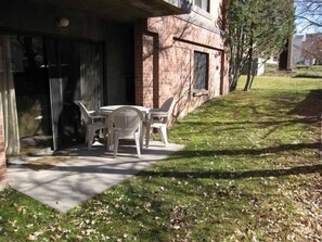 A patio with a table and chairs, a brick building, and a grassy area with fallen leaves.