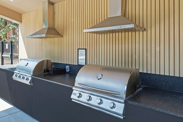 Una zona de cocina al aire libre con una parrilla, extractor de humos y un lavamanos integrado.