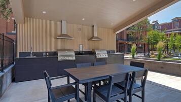 An outdoor kitchen with a table and chairs, a grill, and a view of buildings in the background.