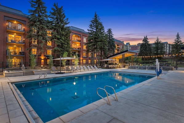 A hotel with a swimming pool, outdoor seating, and a view of the surrounding buildings.