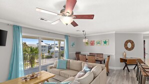 A modern living room with a beige sofa, wooden dining table, and a ceiling fan. - Spacious 3 bed 2.5  ba unit, close to the beach, heated pool, tennis, pickle bal (Santa Rosa Beach)