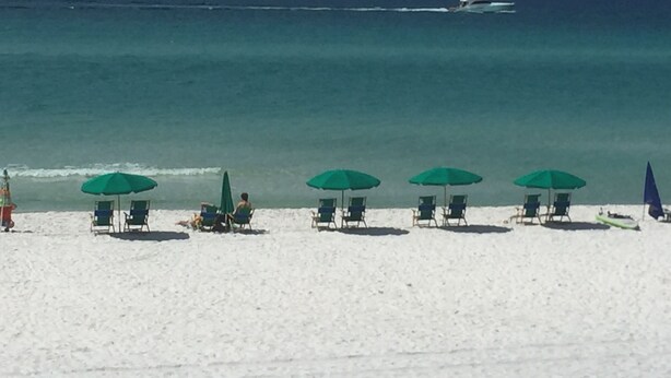 A beach with rows of green umbrellas and beach chairs, a boat in the water, and a clear view of the ocean. - Spacious 3 bed 2.5  ba unit, close to the beach, heated pool, tennis, pickle bal (Santa Rosa Beach)