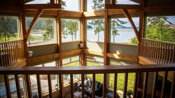 Una cabaña de madera con balcón que da a un lago, con una zona de estar con mesa y sillas.