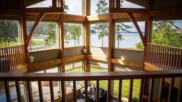 Une cabane en bois dotée d’un balcon donnant sur un lac, et comprenant un espace salon avec une table et des chaises.