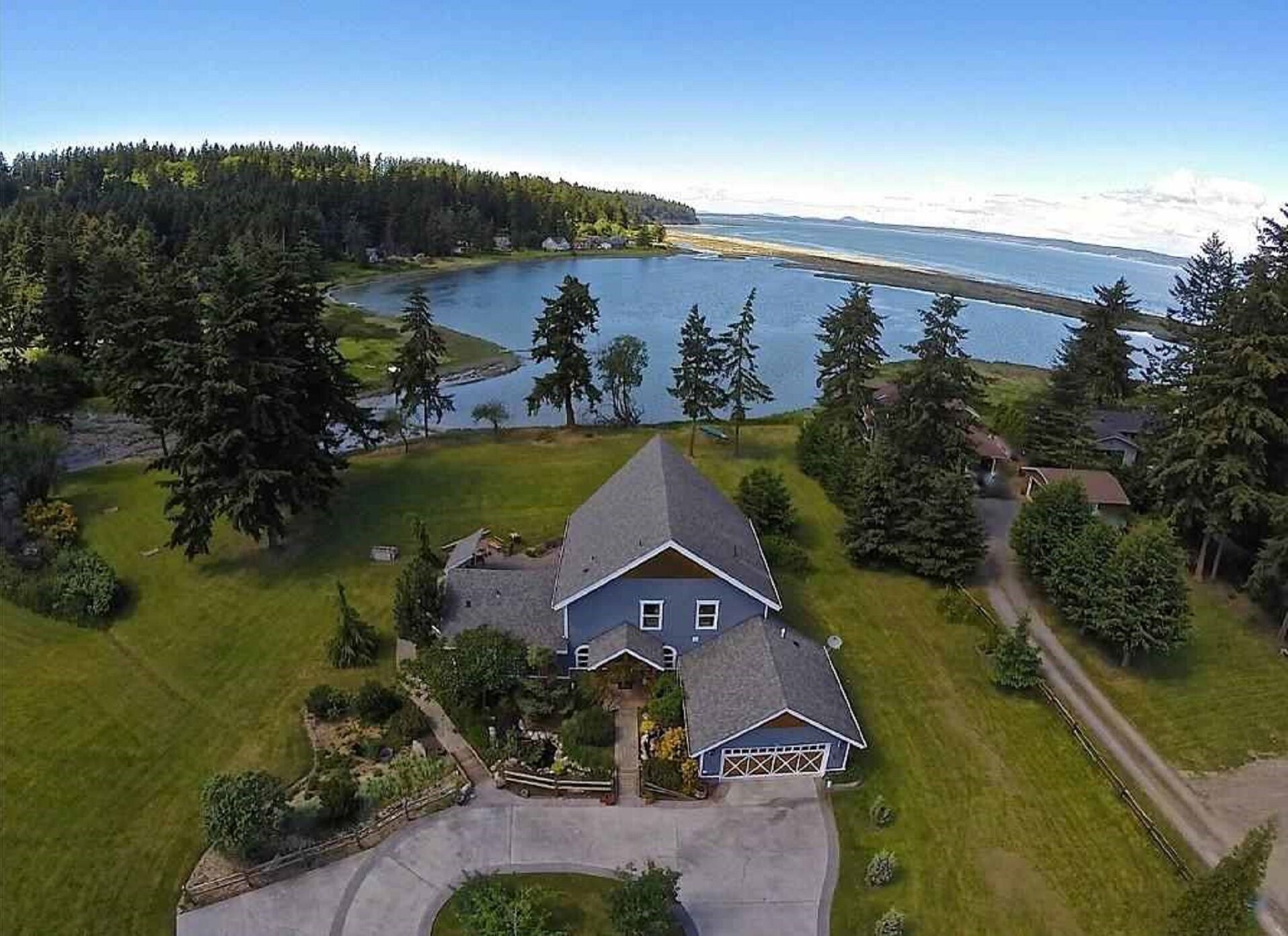 Une grande maison avec un garage, entourée d’une pelouse bien entretenue et d’arbres, située près d’un lac.