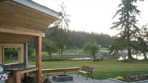 Un patio con piso de madera, una parrilla y un banco con vista a un río y zona boscosa.