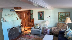 Un salon chaleureux avec une cheminée, un escalier, un canapé bleu, un tapis à motifs et une table basse.
