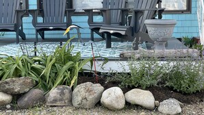 Une véranda avec des fauteuils Adirondack, une sculpture d’oiseau et un jardinière en pierre.