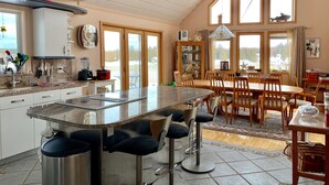 Una cocina amplia con una isla central, taburetes de bar y un comedor con sillas y una mesa de madera.