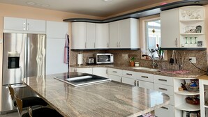 Una cocina moderna con armarios blancos, un refrigerador de acero inoxidable, un microondas y una encimera de granito.