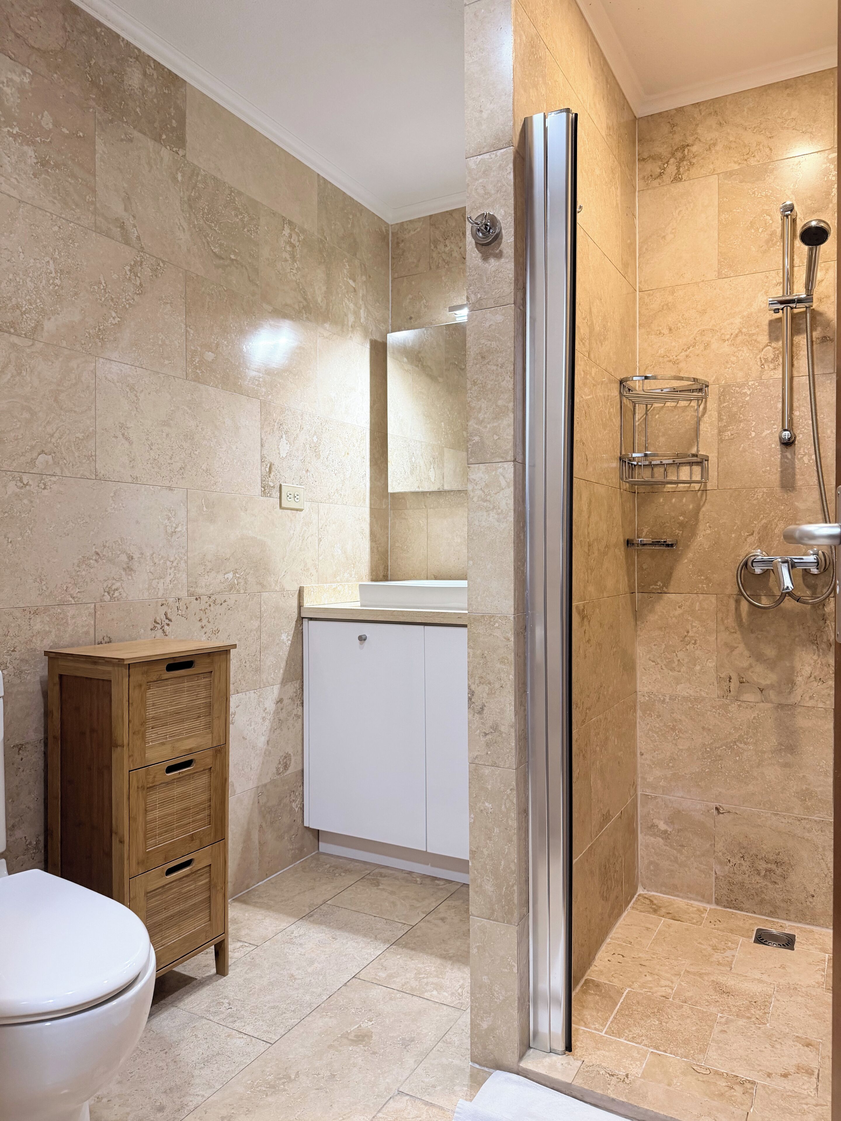 Un baño con ducha, inodoro y armario de madera.