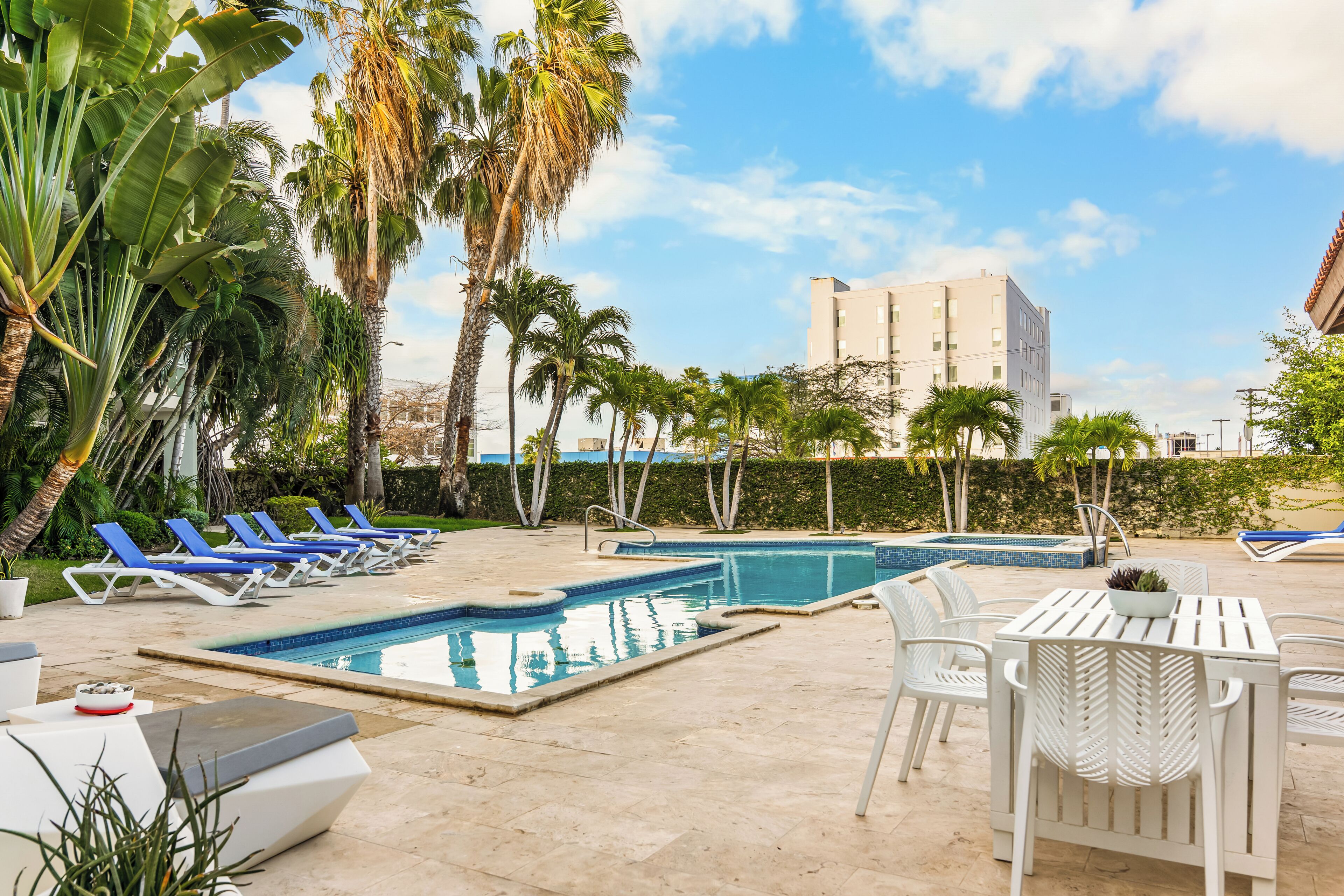 A pool area with lounge chairs, a table, and a building in the background.