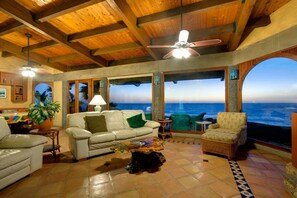 A spacious living room with a view of the ocean, a ceiling fan, and a dining area with a table and chairs. - Security 'Exclusive' Gated Beachfront Private Steps to Beach! Rosarito Beach 🌊
 (Playas de Rosarito)