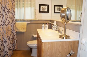 A bathroom with a wooden vanity, a sink, a mirror, and a toilet. There are framed pictures on the wall and a towel hanging on the wall.