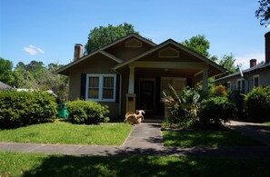 A single-story house with a front porch, a small front yard, and a dog in the driveway.