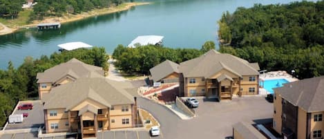 A hotel with a swimming pool, parking lot, and a view of a lake.