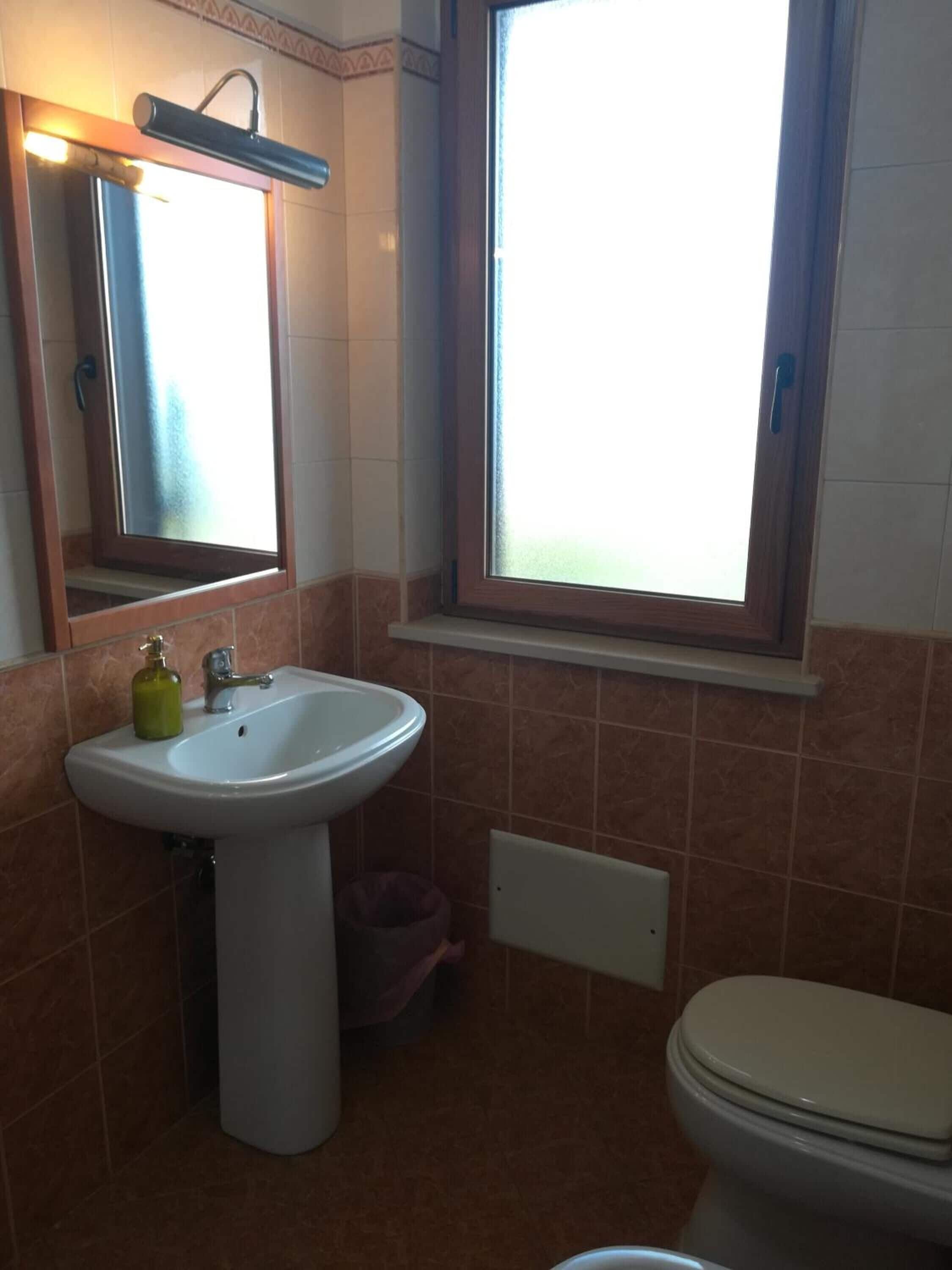 Baño con lavamanos, espejo, ventana y retrete.