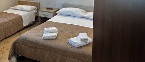 A hotel room with two beds, each with a headboard, a nightstand, and a wall-mounted light. The room has a textured wall and a door with the number 2.