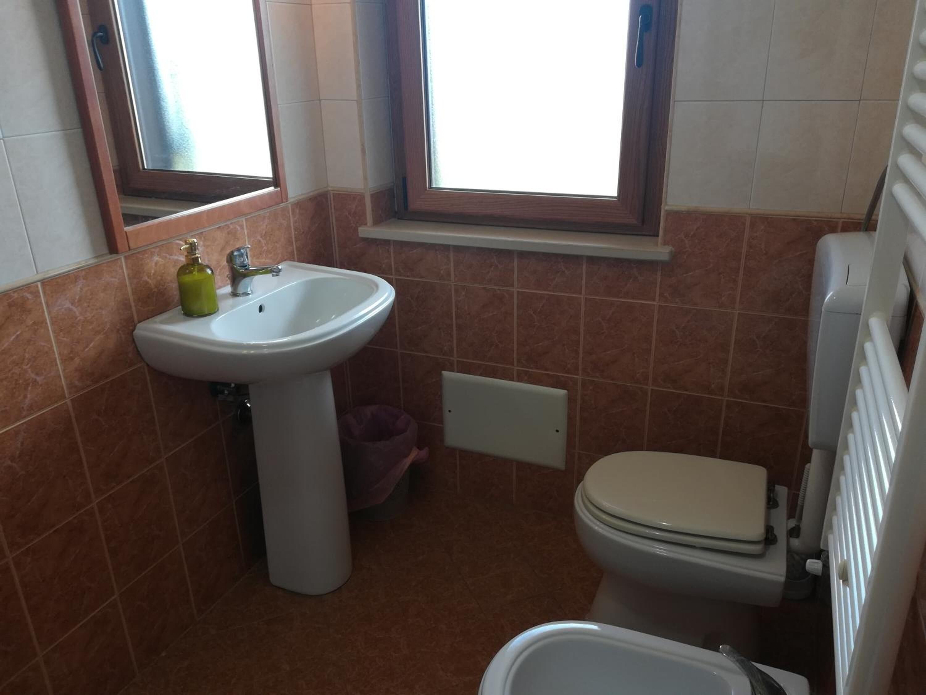 Une petite salle de bain avec un lavabo sur colonne, des toilettes et une fenêtre au-dessus du lavabo.