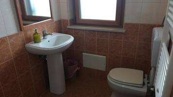 Une petite salle de bain avec un lavabo sur colonne, des toilettes et une fenêtre au-dessus du lavabo.