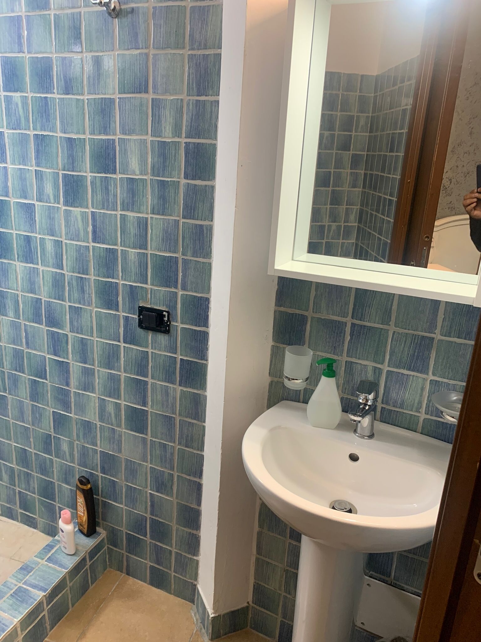 Une salle de bain avec des carreaux de mosaïque bleus, un lavabo blanc, un miroir et des articles de toilette posés sur le comptoir.