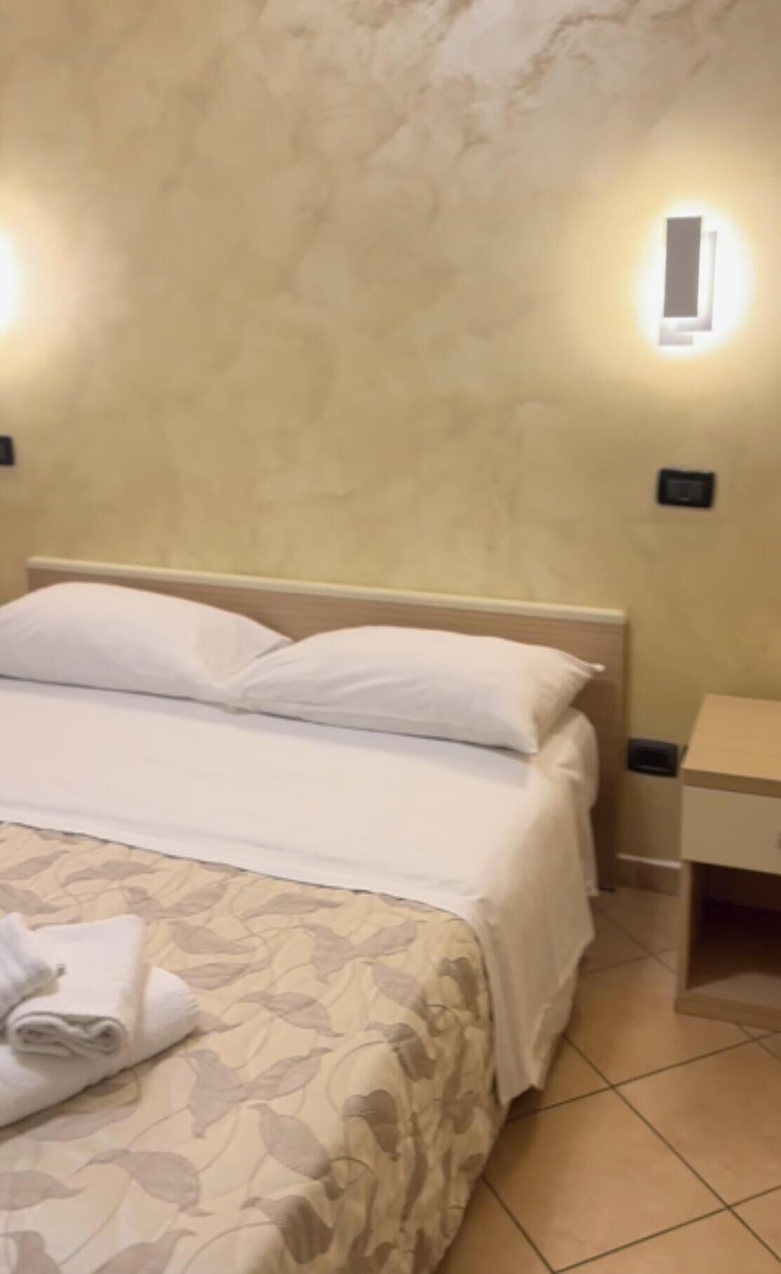 Una habitación de hotel con una cama, una mesita de noche y un aire acondicionado instalado en la pared.
