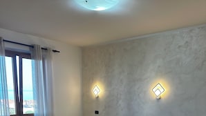 Hotellihuoneessa on kaksi sänkyä, työpöytä ja tuoli. Seinille on asennettu valaisimia, ja ikkunassa on verhot.