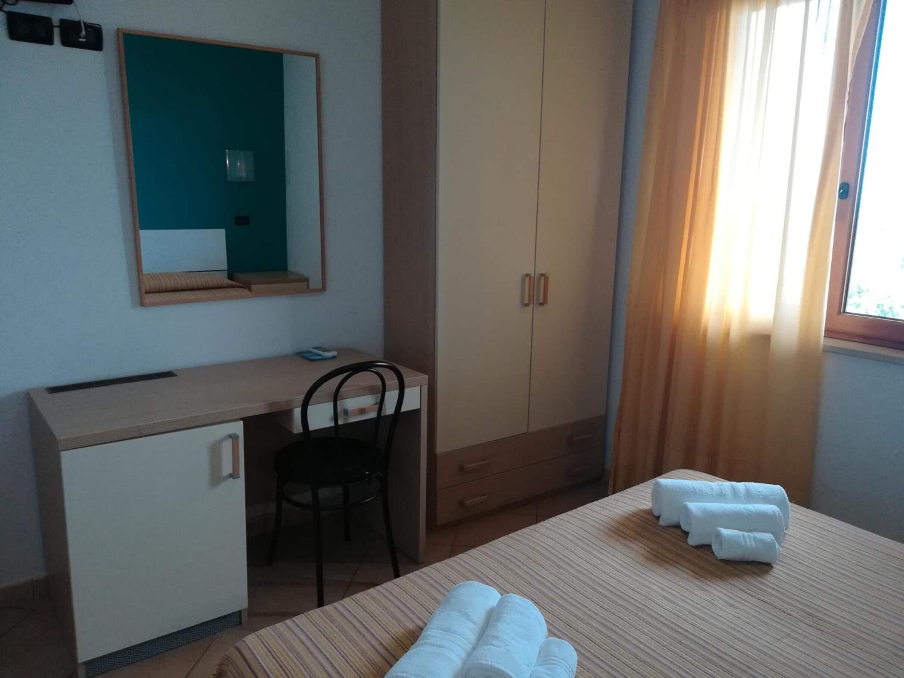 A hotel room with a bed, a desk, a chair, a wardrobe, and a window with curtains.